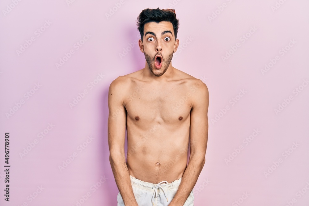 Fototapeta premium Young hispanic man wearing swimwear shirtless afraid and shocked with surprise expression, fear and excited face.