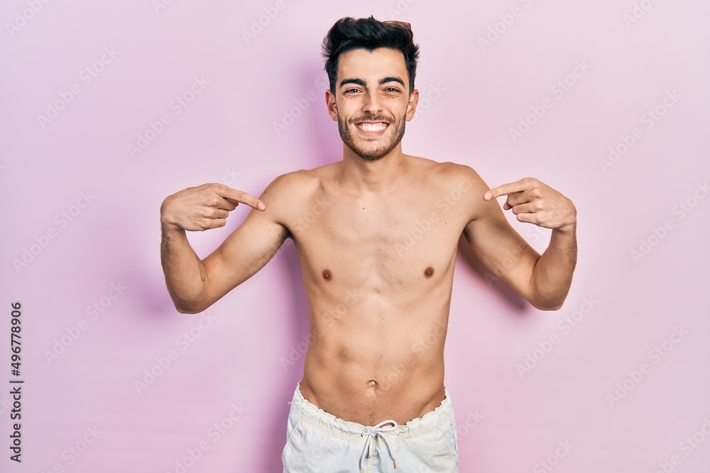 Fototapeta premium Young hispanic man wearing swimwear shirtless looking confident with smile on face, pointing oneself with fingers proud and happy.