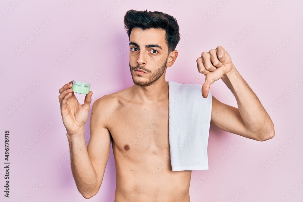 Fototapeta premium Young hispanic man shirtless wearing towel and eye bags patches with angry face, negative sign showing dislike with thumbs down, rejection concept