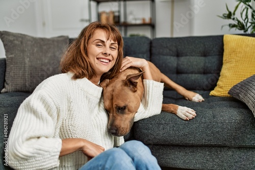Young caucasian woman smiling confident hugging dog sitting on floor at home