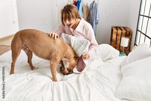 Young caucasian woman smiling confident playing with dog sitting on bed at bedroom