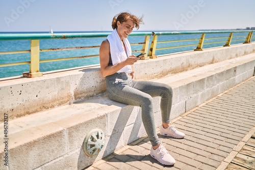 Young caucasian woman wearing sportswear using smartphone at seaside