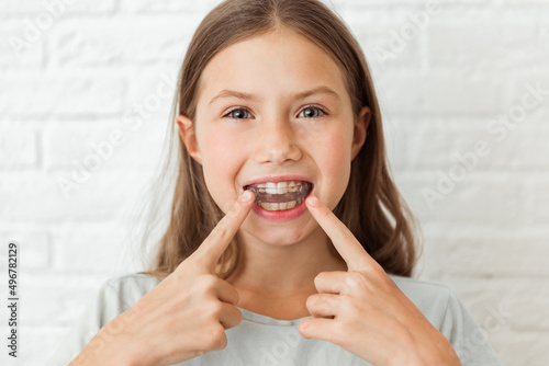 Attractive little girl shows index fingers myofunctional trainer. Help equalize the growing teeth and correct bite, develop mouth breathing habit. Corrects the position of the tongue photo