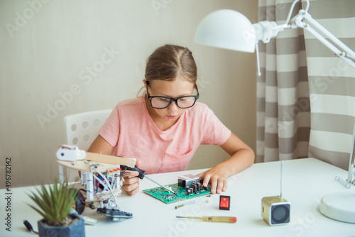 Cute girl constructs metal robot and program it. The boards and microcontrollers are on the table. STEM education inscription. Programming. Mathematics. The science. Technologie. DIY