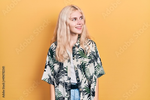 Beautiful caucasian woman with blond hair wearing tropical shirt looking away to side with smile on face, natural expression. laughing confident.