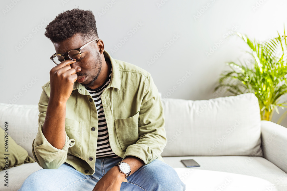 Shot of a young man looking stressed out at home. Frustrated handsome young man touching his head and keeping eyes closed while sitting on the couch at home Shot of a young man looking stressed out at home. Frustrated handsome young man touching his head and keeping eyes closed while sitting on the couch at home