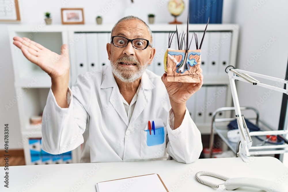Mature doctor man holding model of human anatomical skin and hair celebrating victory with happy smile and winner expression with raised hands Mature doctor man holding model of human anatomical skin and hair celebrating victory with happy smile and winner expression with raised hands