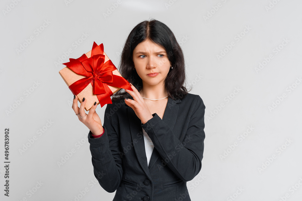 Picky and ignorant displeased spoilt brunette teen girl, holding wrapped cute box with gift, looking with scorn and disappointment at present, white background. Holidays, celebration, birthday concept Picky and ignorant displeased spoilt brunette teen girl, holding wrapped cute box with gift, looking with scorn and disappointment at present, white background. Holidays, celebration, birthday concept
