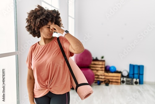 African american woman with afro hair holding yoga mat at pilates room smelling something stinky and disgusting, intolerable smell, holding breath with fingers on nose. bad smell photo