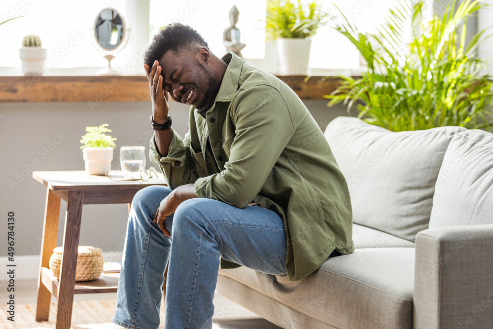 Man looking depressed while sitting alone with his head in his hand on his living room sofa at home. Man sitting alone at home looking sad and distraught