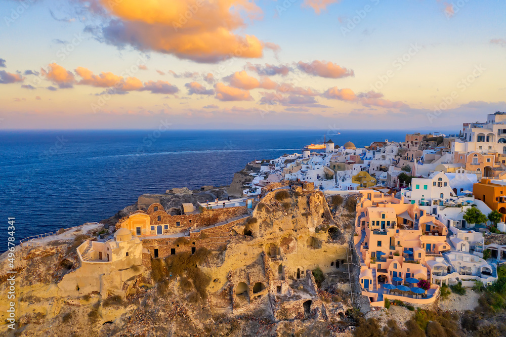 Oia village with traditional white houses, windmills and castle during colorful sunrise. Santorini island, Greece.