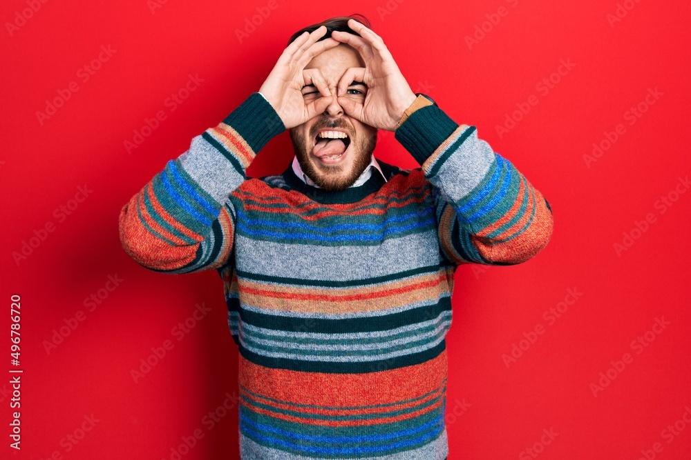 Handsome caucasian man with beard wearing elegant wool winter sweater doing ok gesture like binoculars sticking tongue out, eyes looking through fingers. crazy expression. Handsome caucasian man with beard wearing elegant wool winter sweater doing ok gesture like binoculars sticking tongue out, eyes looking through fingers. crazy expression.