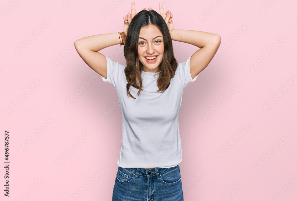Young beautiful woman wearing casual white t shirt posing funny and crazy with fingers on head as bunny ears, smiling cheerful Young beautiful woman wearing casual white t shirt posing funny and crazy with fingers on head as bunny ears, smiling cheerful