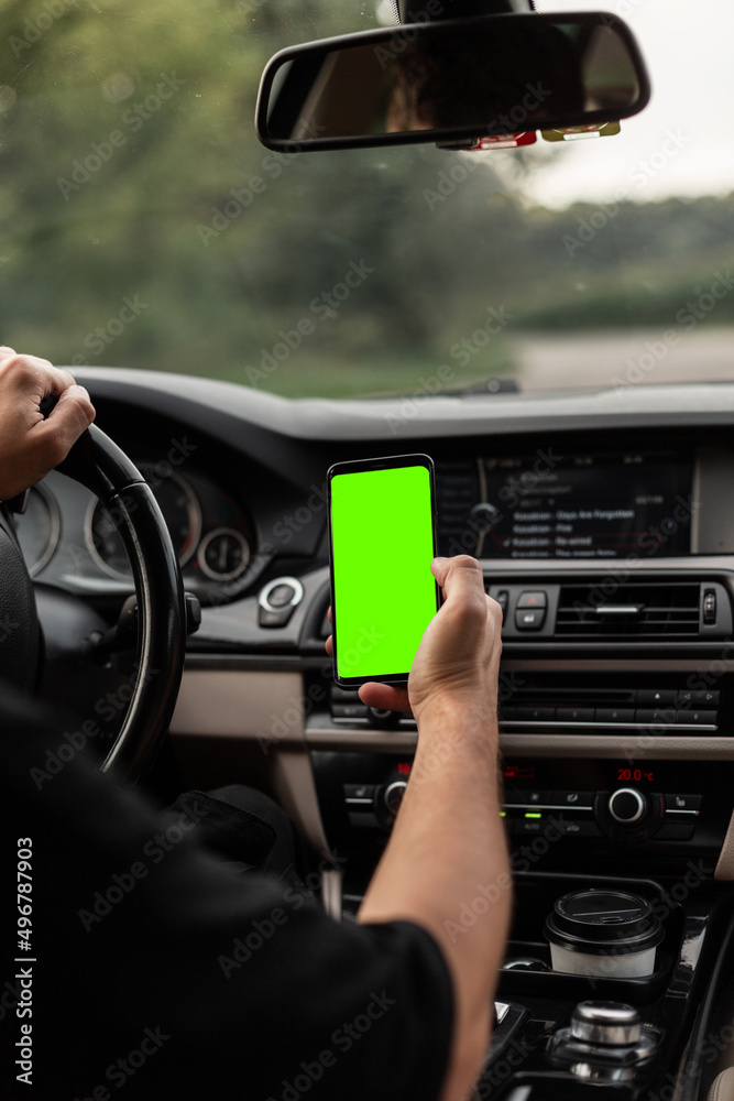 Man driver is driving and holding a smartphone with a green mockup display. Man driver is driving and holding a smartphone with a green mockup display.