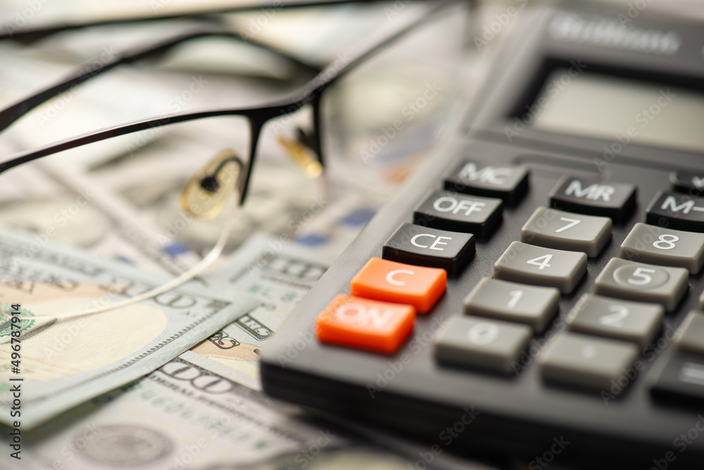 Close up photo of calculator and eyeglasses on dollar bills Close up photo of calculator and eyeglasses on dollar bills