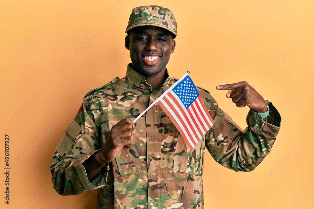 Fototapeta premium Young african american man wearing army uniform holding american flag smiling happy pointing with hand and finger