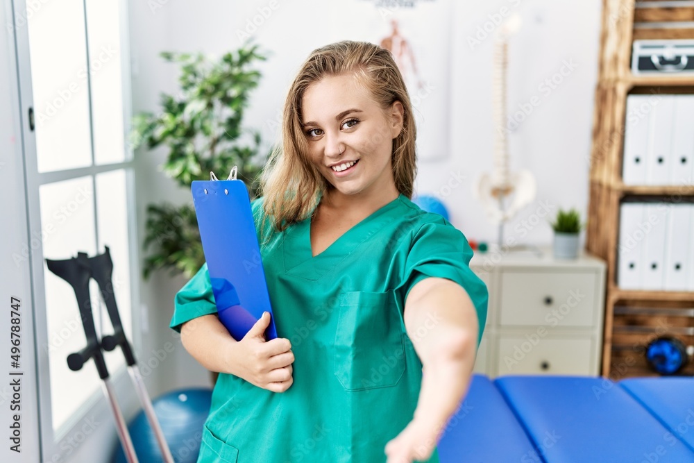 Young caucasian woman working at pain recovery clinic smiling friendly offering handshake as greeting and welcoming. successful business. Young caucasian woman working at pain recovery clinic smiling friendly offering handshake as greeting and welcoming. successful business.