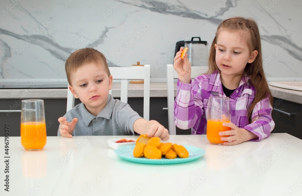 Teenage children eat junk food at home. The child independently eats chicken nuggets at home in the white kitchen Teenage children eat junk food at home. The child independently eats chicken nuggets at home in the white kitchen