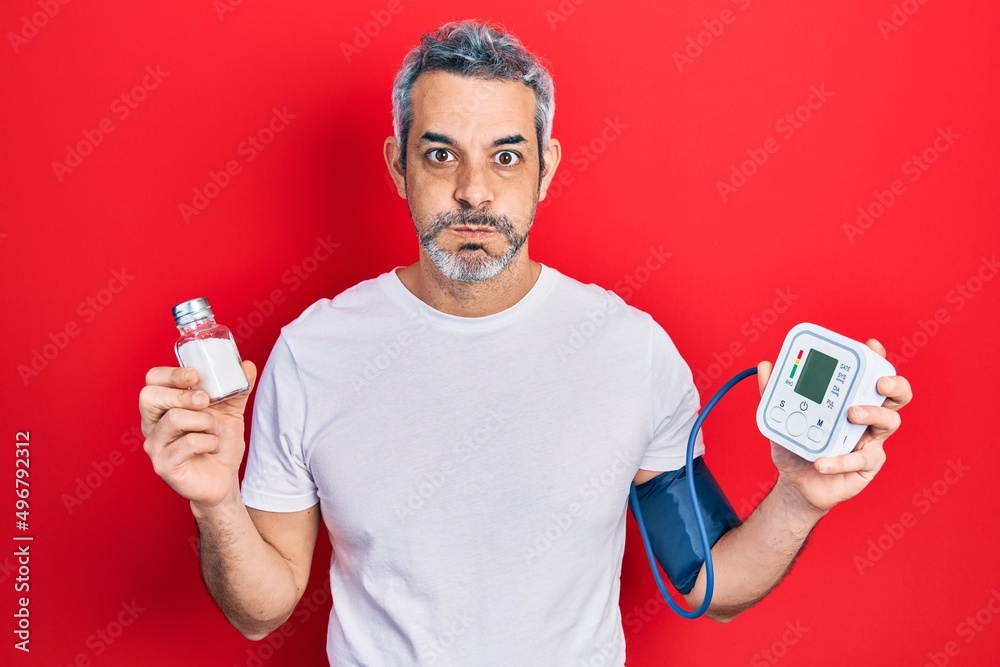 Handsome middle age man with grey hair using blood pressure monitor