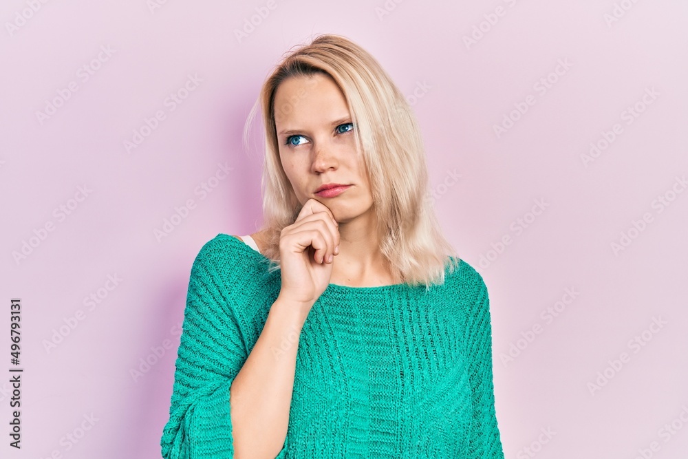 Beautiful caucasian blonde woman wearing casual winter sweater thinking concentrated about doubt with finger on chin and looking up wondering Beautiful caucasian blonde woman wearing casual winter sweater thinking concentrated about doubt with finger on chin and looking up wondering