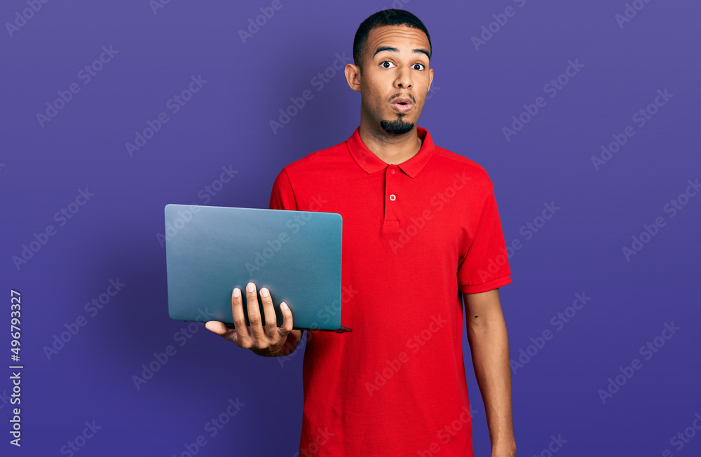 Young african american man working using computer laptop scared and amazed with open mouth for surprise, disbelief face Young african american man working using computer laptop scared and amazed with open mouth for surprise, disbelief face