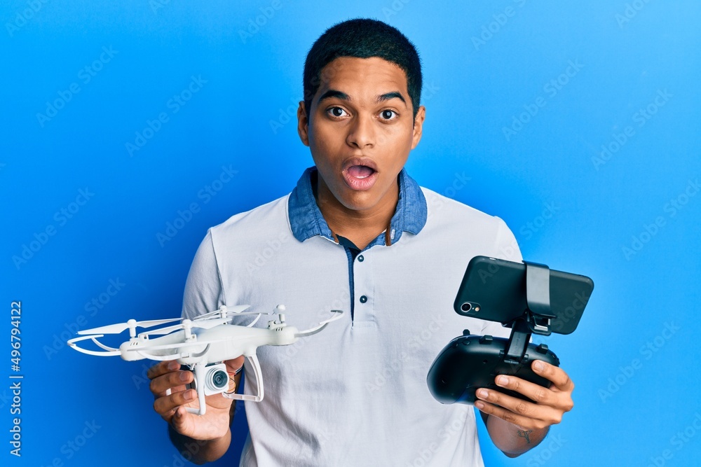 Young handsome hispanic man using drone holding remote control afraid and shocked with surprise and amazed expression, fear and excited face. Young handsome hispanic man using drone holding remote control afraid and shocked with surprise and amazed expression, fear and excited face.