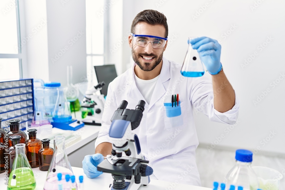 Young hispanic man wearing scientist uniform holding test tube at laboratory Young hispanic man wearing scientist uniform holding test tube at laboratory