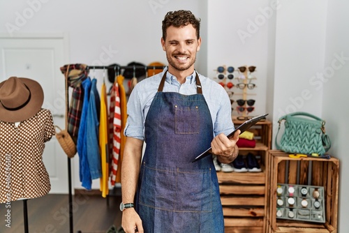 Handsome young man working as manager at retail boutique winking looking at the camera with sexy expression, cheerful and happy face.