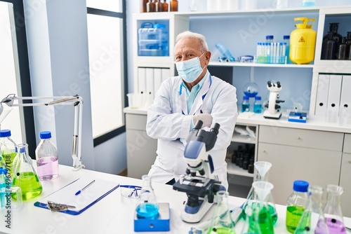Senior man wearing scientist uniform and medical mask with arms crossed gesture at laboratory