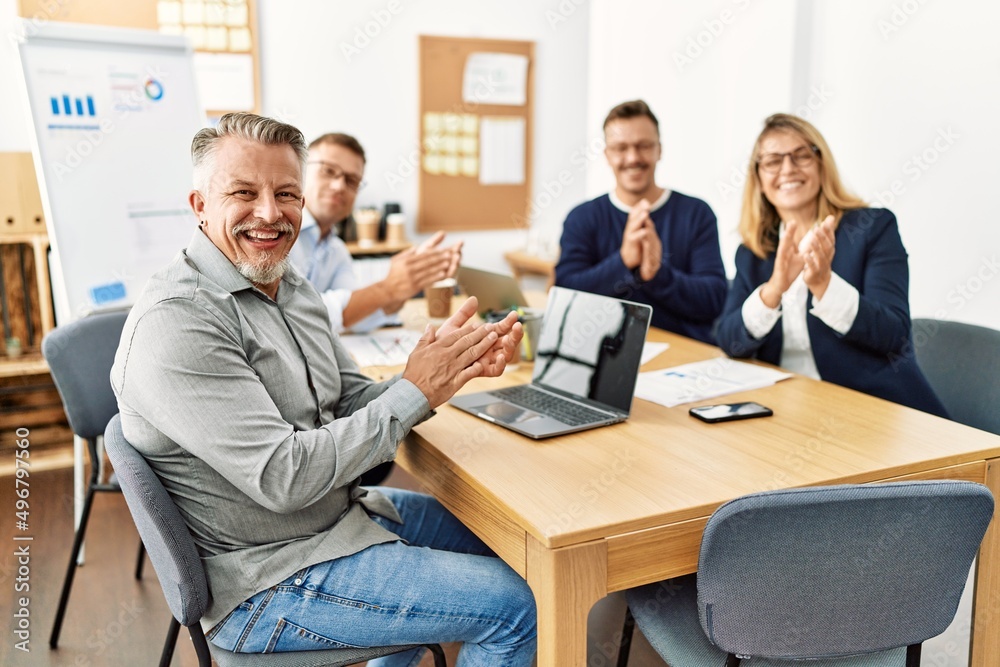 Group of middle age business workers smiling happy. Sitting on the table clapping and looking to the camera at the office.