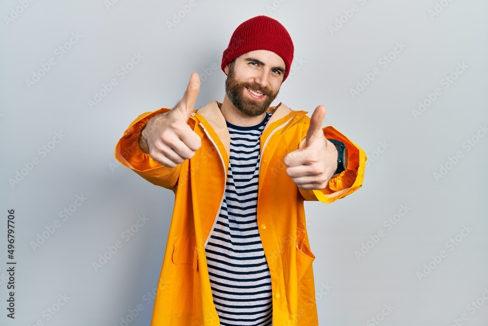 Caucasian man with beard wearing yellow raincoat approving doing positive gesture with hand, thumbs up smiling and happy for success. winner gesture. Caucasian man with beard wearing yellow raincoat approving doing positive gesture with hand, thumbs up smiling and happy for success. winner gesture.