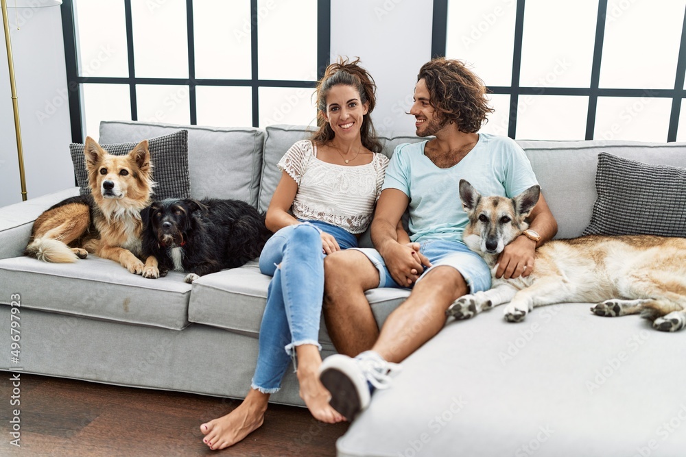 Obraz na plátně Man and woman couple smiling confident sitting on sofa with dogs at home