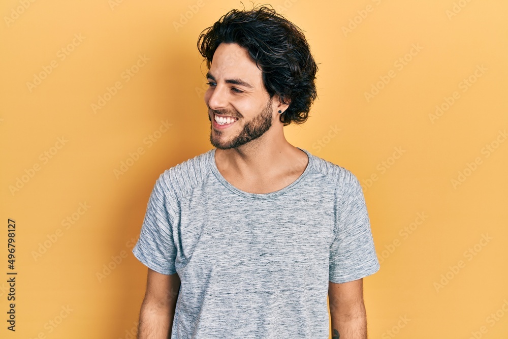 Handsome hispanic man wearing casual grey t shirt looking to side, relax profile pose with natural face and confident smile.