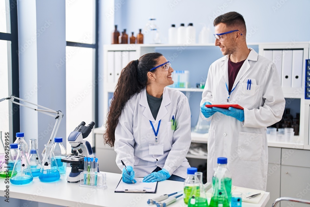 Man and woman wearing scientist uniform using touchpad write on document at laboratory