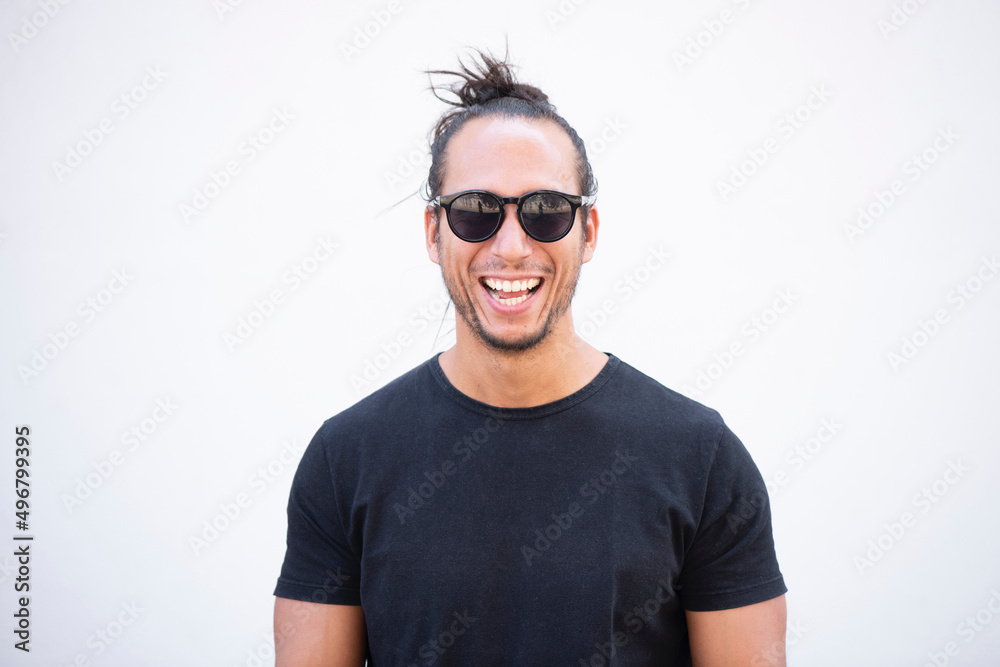 Cheerful handsome man with hair bun and sunglasses against white wall laughing Cheerful handsome man with hair bun and sunglasses against white wall laughing
