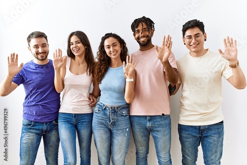 Group of young people standing together over isolated background waiving saying hello happy and smiling, friendly welcome gesture