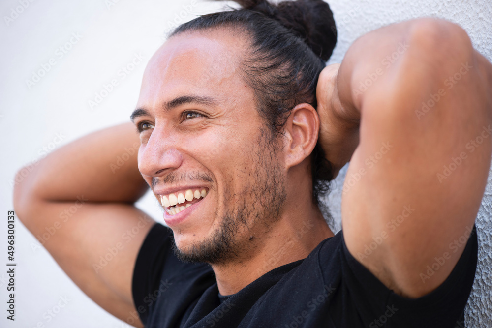Obraz premium Cheerful man with pulled up hair bun and hands behind head over white background