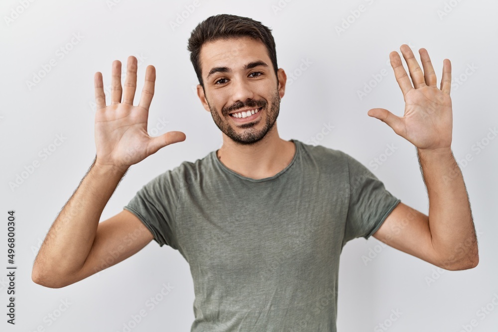Young hispanic man with beard wearing casual t shirt over white background showing and pointing up with fingers number ten while smiling confident and happy. Young hispanic man with beard wearing casual t shirt over white background showing and pointing up with fingers number ten while smiling confident and happy.