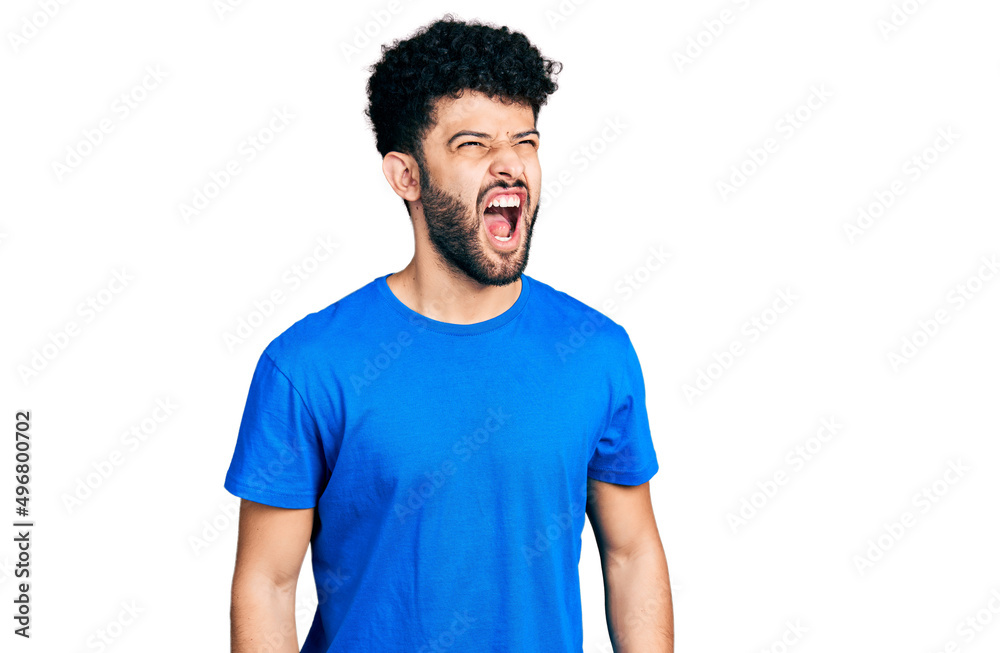 Young arab man with beard wearing casual blue t shirt angry and mad screaming frustrated and furious, shouting with anger. rage and aggressive concept. Young arab man with beard wearing casual blue t shirt angry and mad screaming frustrated and furious, shouting with anger. rage and aggressive concept.