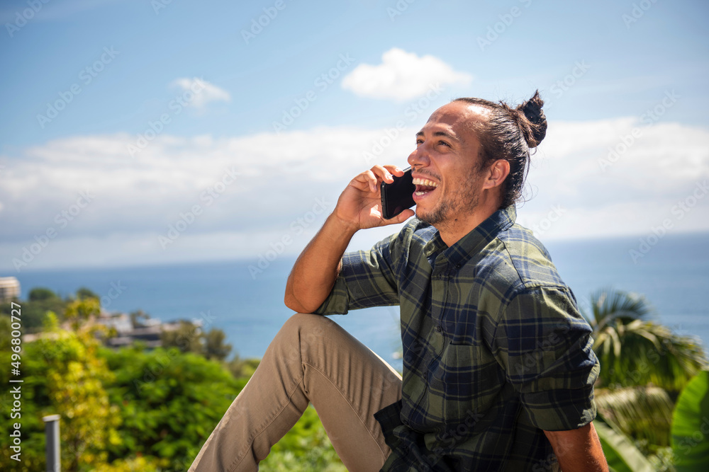 Happy man traveler with pulled up hair bun talking on mobile phone overlooking sea Happy man traveler with pulled up hair bun talking on mobile phone overlooking sea