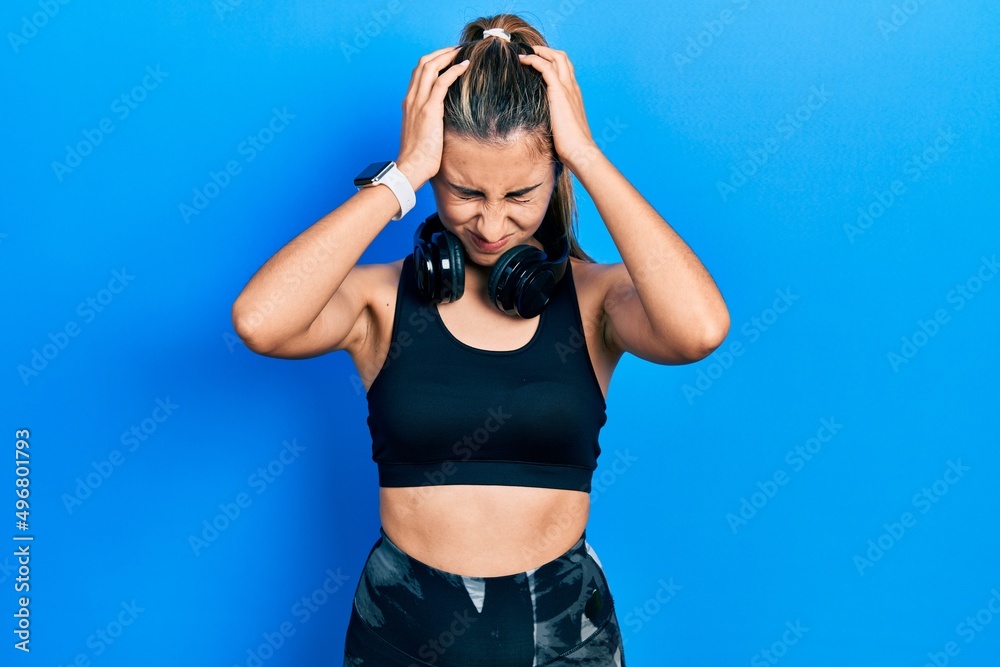 Beautiful hispanic woman wearing gym clothes and using headphones suffering from headache desperate and stressed because pain and migraine. hands on head.