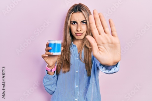 Beautiful hispanic woman holding earwax cotton removers with open hand doing stop sign with serious and confident expression, defense gesture photo