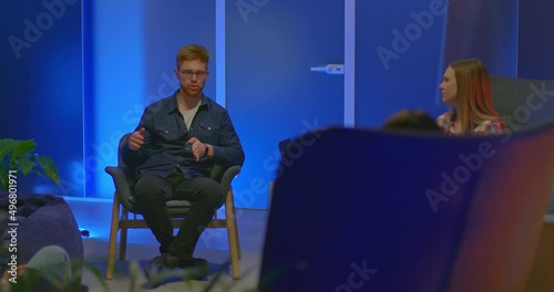Red-haired guy sits in a chair and talks with colleagues, meeting partners. Guy with glasses talks about a new business project, a modern coworking office. 4k, ProRes