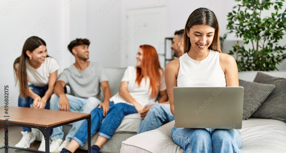 Fototapeta premium Group of young friends speaking sitting on the sofa. Woman smilimg happy and using laptop at home.