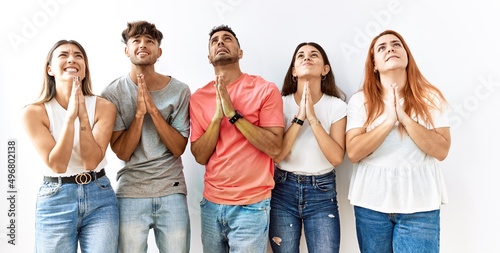 Obraz na plátně Group of young friends standing together over isolated background begging and praying with hands together with hope expression on face very emotional and worried