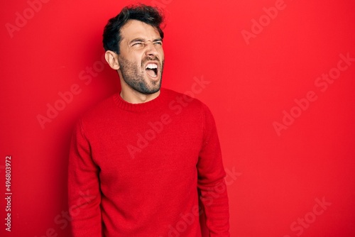 Handsome man with beard wearing casual red sweater angry and mad screaming frustrated and furious, shouting with anger. rage and aggressive concept.