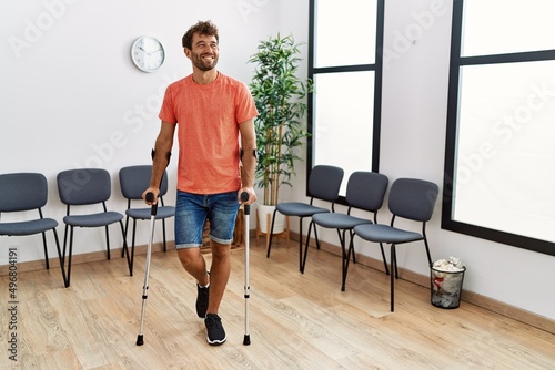 Cuadro en lienzo Young hispanic man walking using crutches at clinic waiting room.