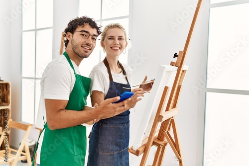 Young artist couple smiling happy using smartphone and painting at art studio.