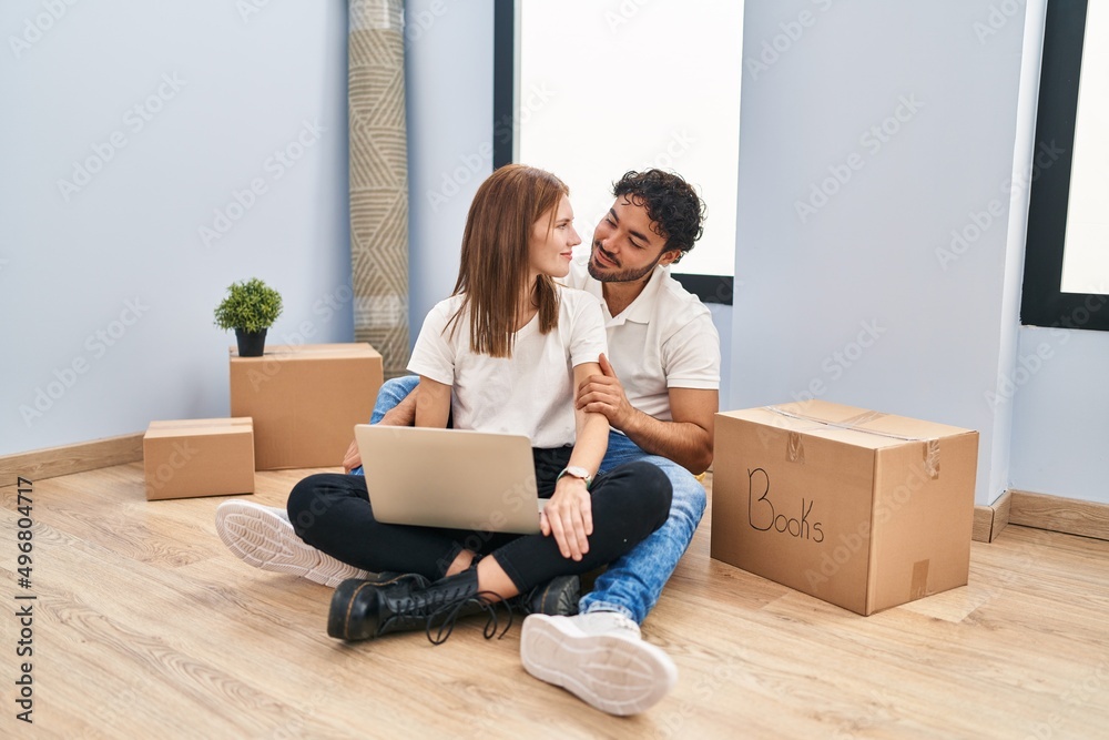 Young couple using laptop at new home looking to side, relax profile pose with natural face and confident smile. Young couple using laptop at new home looking to side, relax profile pose with natural face and confident smile.