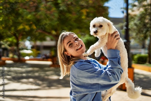 Young blonde girl smiling happy holding dog at the city.